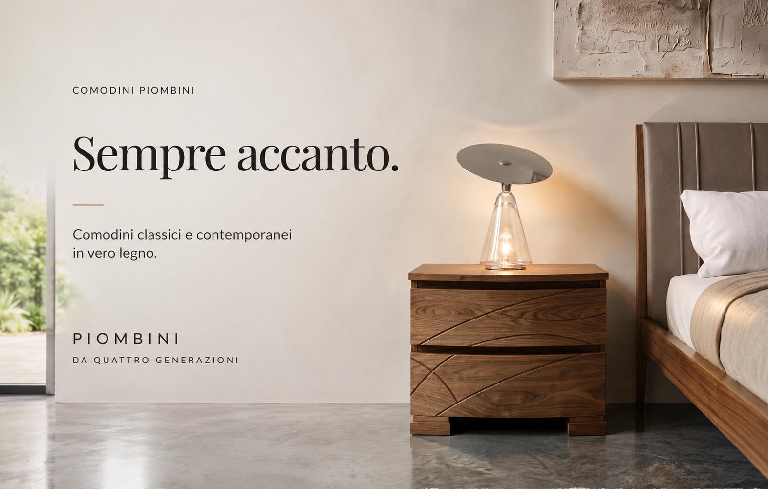 Collezione Comodini Piombini con comodino classico in vero legno accanto al letto, ambiente notte elegante dai toni caldi e messaggio "Sempre accanto.". L'immagine rappresenta la collezione di comodini classici e contemporanei in vero legno.