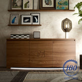 Credenza moderna sagomata a tre ante in elegante legno di noce con illuminazione LED integrata, della collezione Modigliani di Piombini. Design artigianale italiano con intarsio geometrico centrale, ideale per ambienti sofisticati e contemporanei. Mobile di pregio che unisce estetica, funzionalità e tradizione Made in Italy.