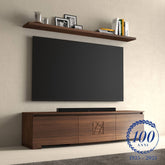 Mobile TV moderno sagomato in legno di noce della collezione Modigliani, con decorazione centrale intagliata, abbinato a mensola sospesa. Televisore a parete e oggetti decorativi su sfondo neutro. Logo celebrativo del centenario 1925–2025 in basso a destra.