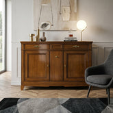 Credenza classica D'Este P3009AL in legno vista di tre quarti, con due porte lisce, tre cassetti e fianco lavorato, ambientata in un soggiorno elegante.