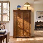 Armadio Dispensa Tiziano RH110 aus Holz, in einem hellen Esszimmer inszeniert, mit zwei Drehtüren, Fischgrätintarsien und warmer klassischer Piombini-Oberfläche.