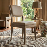 Modern dining chair with canaletto walnut wood frame, lacquered dove grey finish, and dove grey leather upholstery, set in an elegant, bright living room.