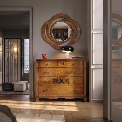 Interior of a luxurious, sophisticated bedroom with a large opening to a walk-in closet, lit by warm sunlight from the right. Centered on a herringbone parquet floor is the Como Classico Five-Drawer Secret dresser from Piombini's Arte d'Este collection, cherry finish. On top are a Flos Snoopy lamp, a glossy red Hermès elephant paperweight, and an oval Classic mirror from the D'Este collection.