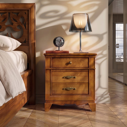 Front view of the classic Arte D'Este Piombini cherrywood bedside table with a Flos KTribe lamp and alarm clock on top. Chevron parquet floor and decorative shadows on the wall.
