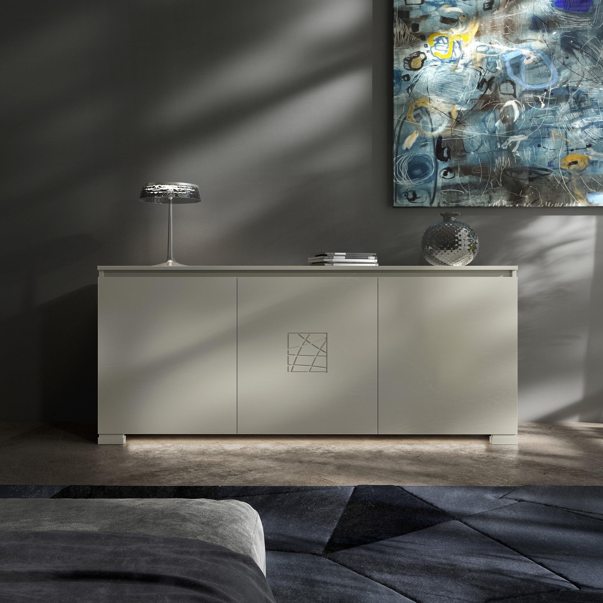 Credenza Modigliani Piombini a 3 ante in finitura Onice con decoro Comete; ambientazione in stile Soft Modern con lampada Flos Bon Jour, vaso Venini Monofiore Balloton fumè, tappeto geometrico blu e divano moderno grigio.