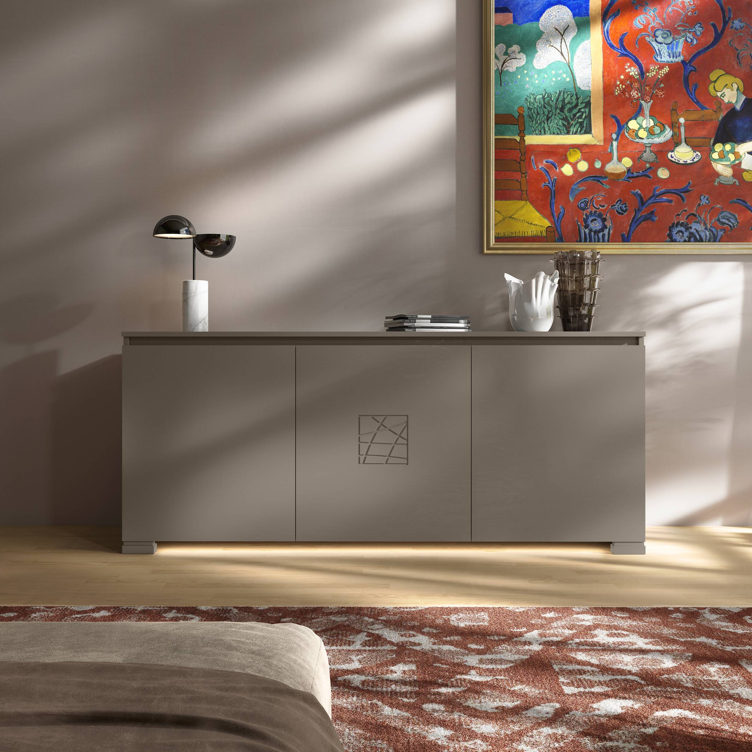 Credenza Modigliani Piombini a 3 ante in finitura Tortora con decoro Comete; ambientazione in stile Soft Luxury con lampada Penta Elisabeth, vaso Venini Fazzoletto, vaso Venini Ritaglio, tappeto contemporaneo rosso e divano moderno beige.
