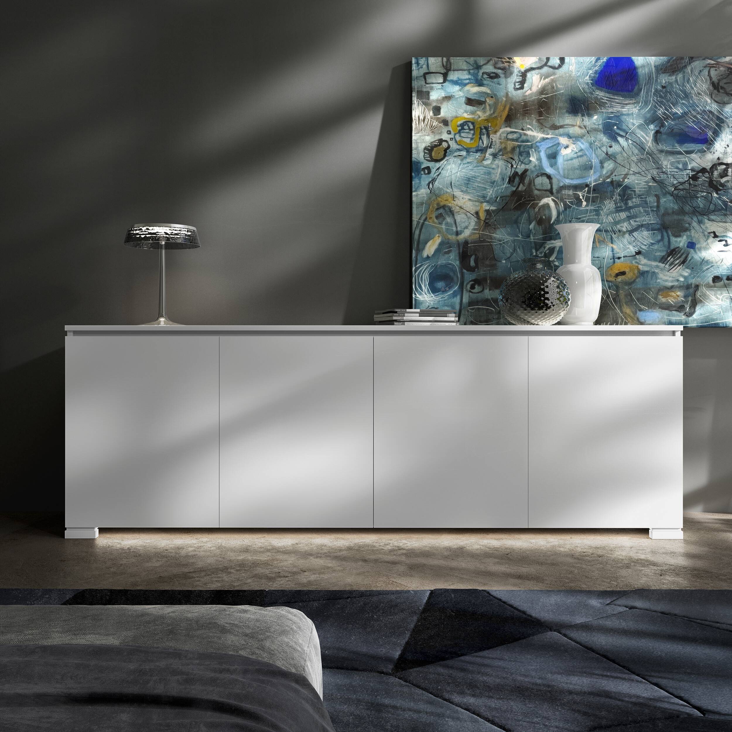 Credenza Modigliani Piombini a 4 ante in finitura Bianco Laccato con anta liscia; ambientazione in stile Soft Modern con lampada Flos Bon Jour, vaso Venini Monofiore Balloton fumè, vaso Venini Opalino, tappeto geometrico blu e divano moderno grigio.