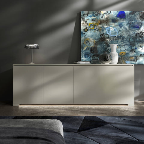 Credenza Modigliani Piombini a 4 ante in finitura Onice Laccato con anta liscia; ambientazione in stile Soft Modern con lampada Flos Bon Jour, vaso Venini Monofiore Balloton fumè, vaso Venini Opalino, tappeto geometrico blu e divano moderno grigio.