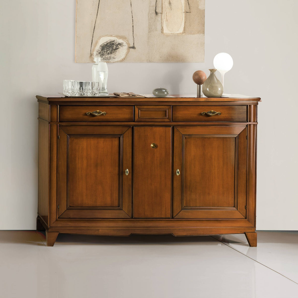 Credenza classica in legno di ciliegio con due ante laterali e un vano centrale portabottiglie, elegantemente nascosto. Completano il mobile tre cassetti superiori, di cui uno centrale segreto, perfettamente integrato nel design. Collezione Arte d’Este Piombini.