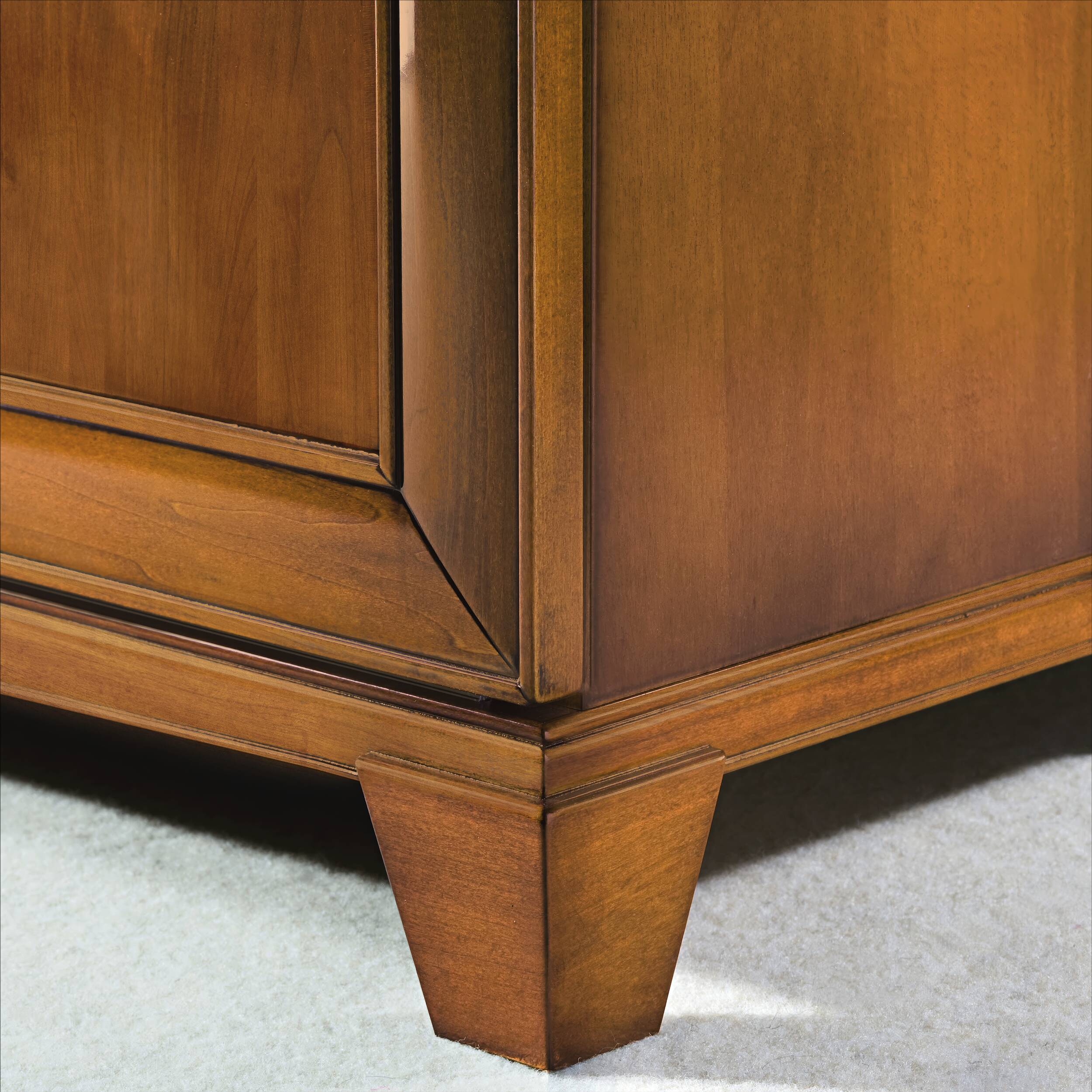 Dettaglio del basamento della credenza classica Piombini, modello P3010 della collezione Arte d’Este, in finitura GRN14 Bassano chiaro anticato. Si evidenziano le gambe rastremate, il taglio angolato delle cornici e la venatura naturale del legno massello