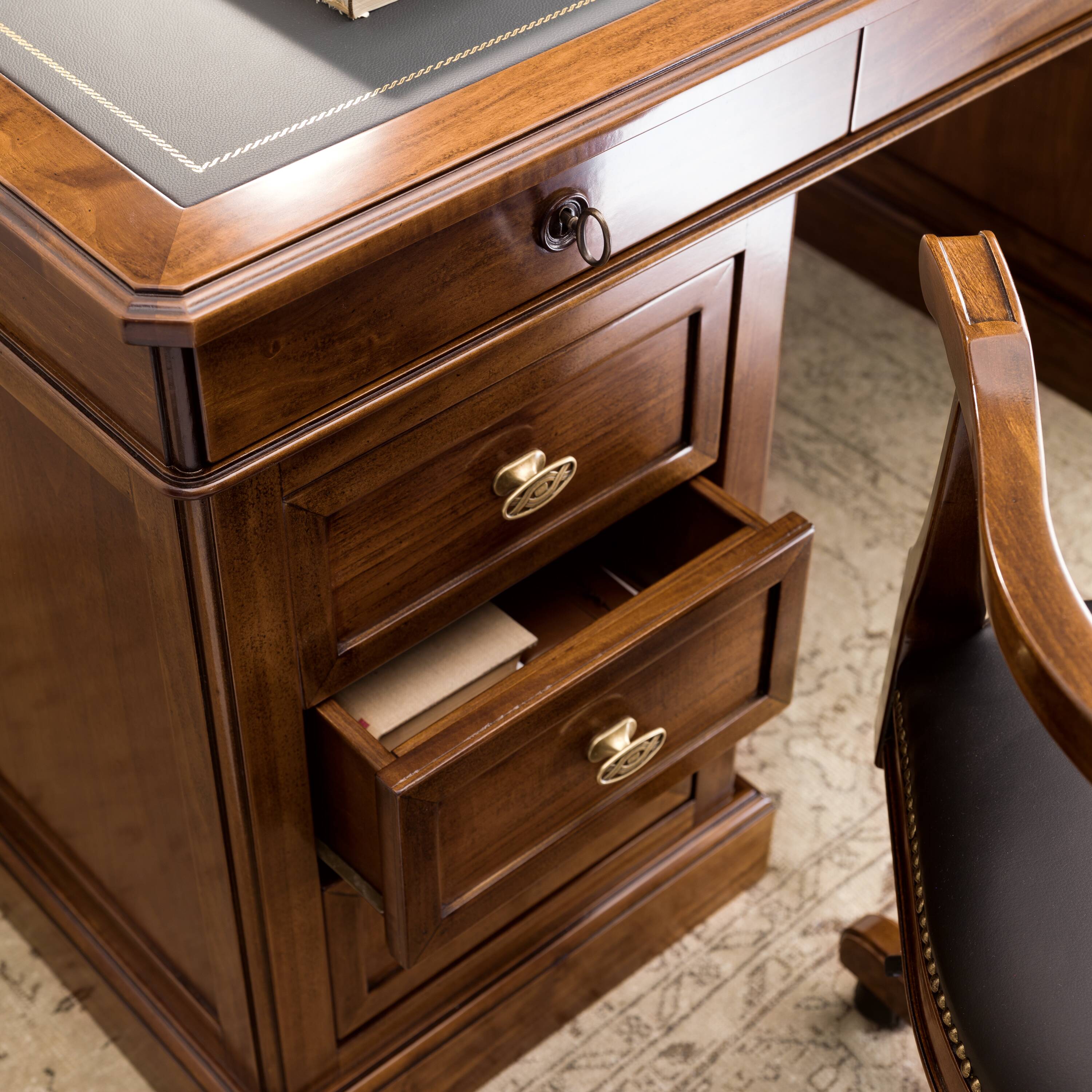 La bellezza si cela nei particolari autentici: la scrivania 8840 / 8841 presenta cassetti laterali dal profilo sagomato, valorizzati dal classico pomolo della Collezione Arte. Il piano, rivestito in Vera Pelle, è impreziosito da una lavorazione artigianale con decoro stampato a mano in autentica foglia oro. Un’eleganza senza tempo che dialoga con la solidità del legno di ciliegio e la funzionalità dei cassetti profondi con serratura a chiave.