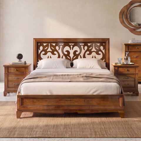 Letto matrimoniale classico D’Este in legno, visto frontalmente tra i due comodini. La grande testata traforata disegna forme morbide e simmetriche, lasciando passare la luce tra pieni e vuoti. Le calde venature del legno incorniciano il letto e trasmettono alla stanza una sensazione di equilibrio, intimità e quiete.