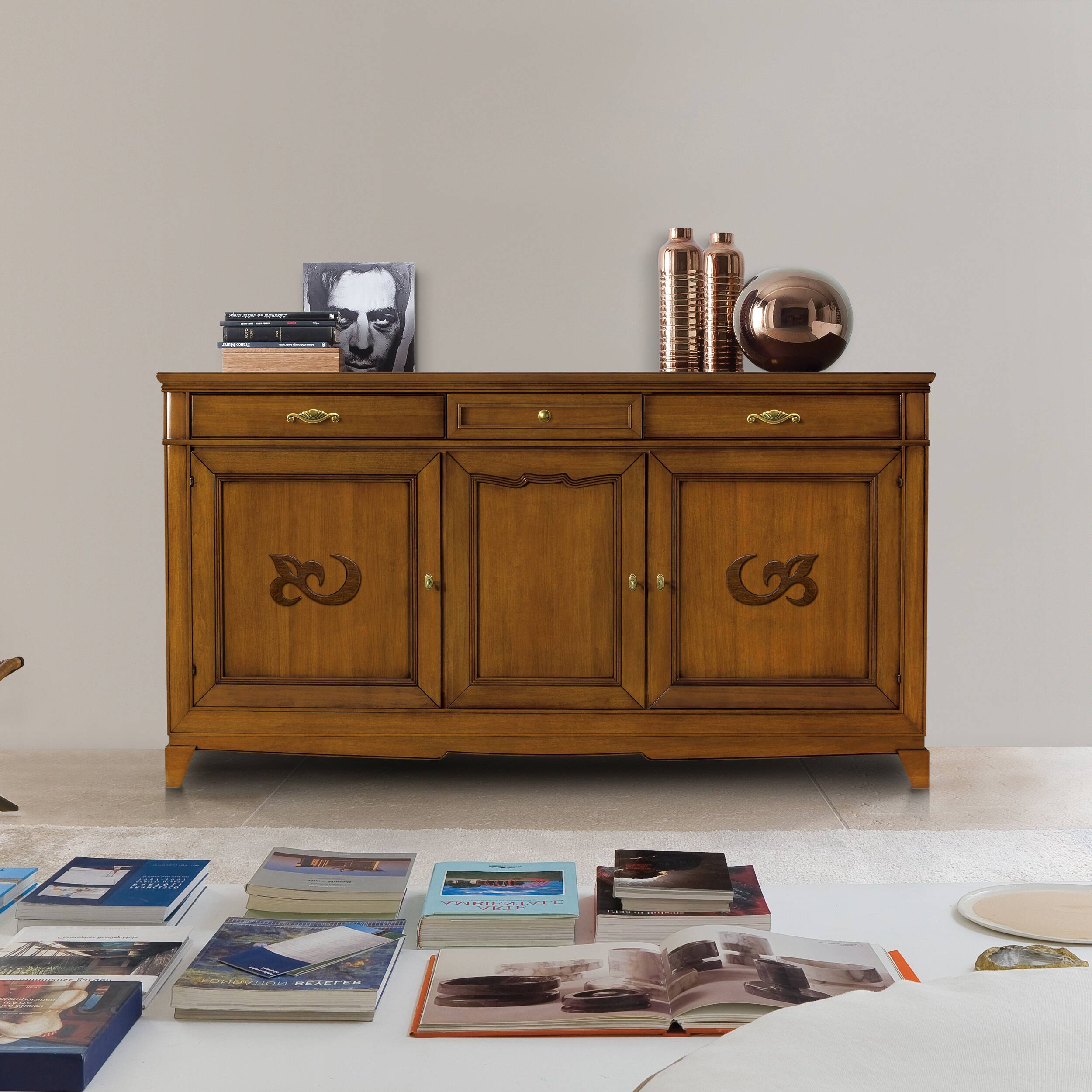 Credenza classica D'Este P3003 in legno, con tre porte decorate, tre cassetti e finitura calda effetto ciliegio, ambientata in un elegante soggiorno.