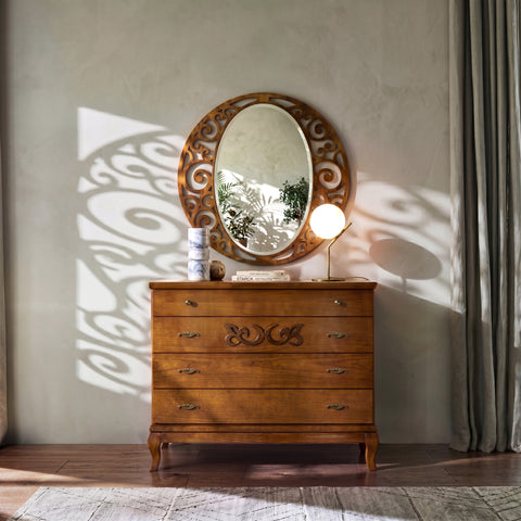 Comò D’Angiò in legno con quattro cassetti e decoro centrale sul frontale; sopra il piano, una specchiera ovale con cornice traforata.