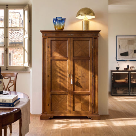 Armadio Dispensa Tiziano RH110 in legno, ambientato in una sala da pranzo luminosa, con due ante battenti, intarsio a spina di pesce e calda finitura classica Piombini.