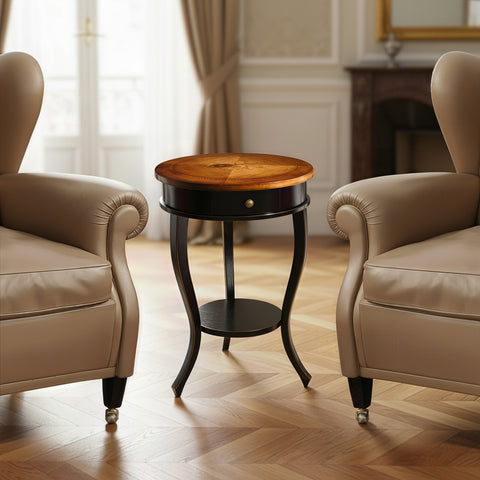 Il tavolino rotondo Tiziano nella finitura Nero Bicolore si distingue per il piano in legno di noce finemente intarsiato, in contrasto con le gambe sagomate scure. Accanto alle poltrone, le proporzioni leggere e il calore del legno creano un ambiente raccolto, elegante e armonioso.