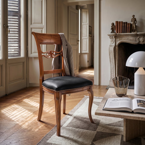 Sedia classica Vittoria in legno massello con seduta imbottita rivestita in vera pelle Siviglia Top Nero, inserita in un ambiente elegante e luminoso con pavimento in legno e camino in pietra
