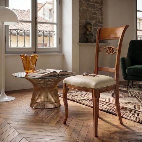 Sedia classica Vittoria in legno massello con seduta imbottita rivestita in vera pelle Siviglia Top Crema, inserita in un ambiente elegante con pavimento in legno, tavolino in vetro e luce naturale