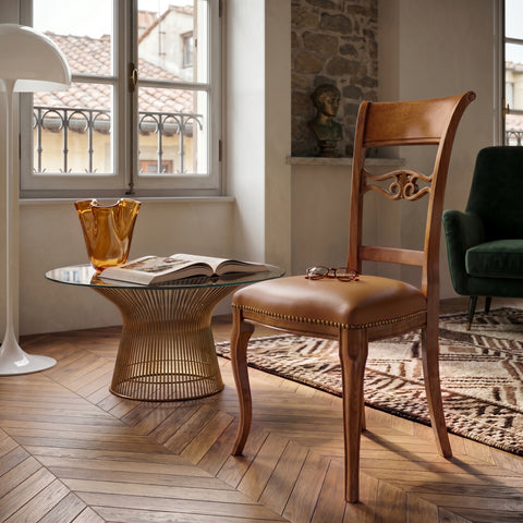 Sedia classica Vittoria in legno massello con seduta imbottita rivestita in vera pelle Siviglia Top Biscotto, ambientata in un soggiorno elegante con pavimento in legno, tavolino in vetro e luce naturale