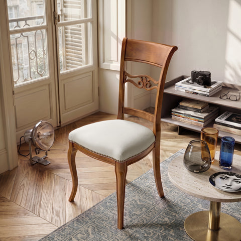 Sedia classica Vittoria in legno massello con seduta imbottita rivestita in vera pelle Siviglia Top Bianco, ambientata in un soggiorno elegante con pavimento in legno, tavolino moderno e luce naturale