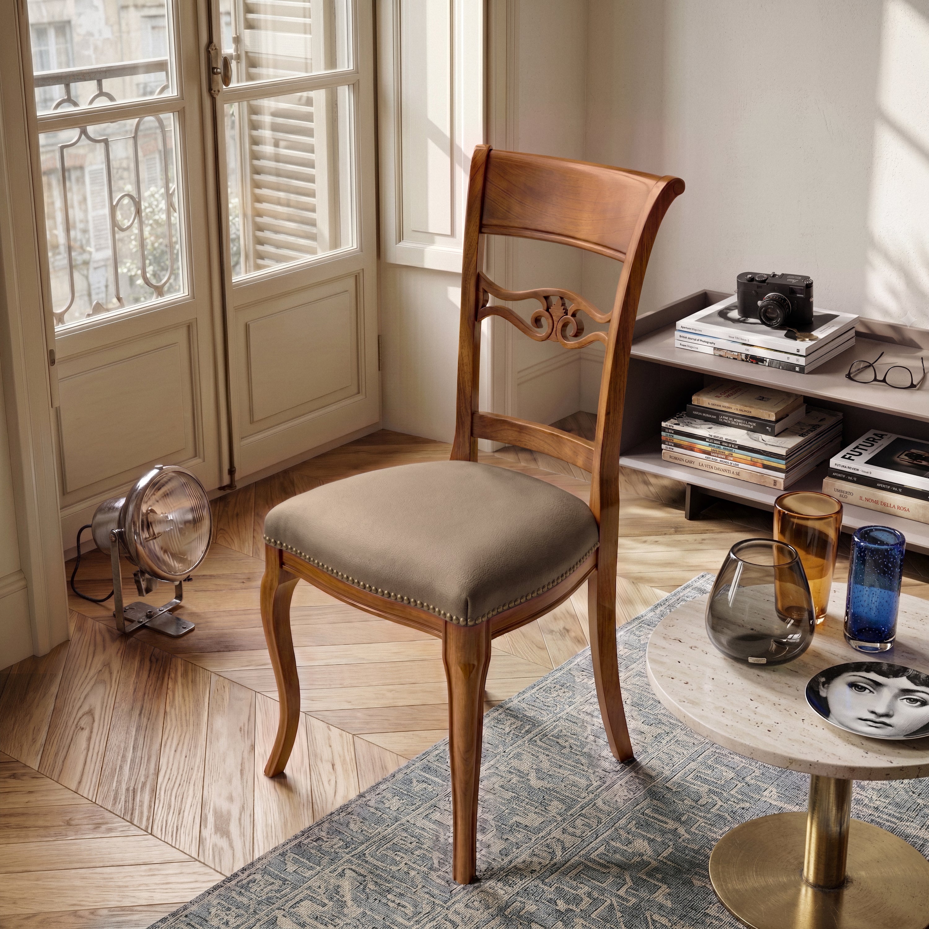 Sedia classica Vittoria in legno massello con seduta imbottita rivestita in vera pelle Siviglia Top Tortora, inserita in un ambiente elegante con pavimento in legno, tavolino moderno e luce naturale