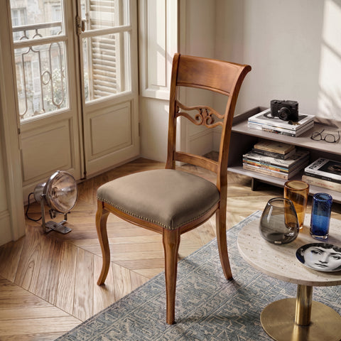 Sedia classica Vittoria in legno massello con seduta imbottita rivestita in vera pelle Siviglia Top Tortora, inserita in un ambiente elegante con pavimento in legno, tavolino moderno e luce naturale