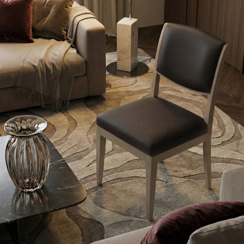 Sedia da pranzo moderna con struttura in legno di noce canaletto Laccato Tortora e rivestimento in pelle Testa di Moro, ambientata in un salotto elegante e luminoso.