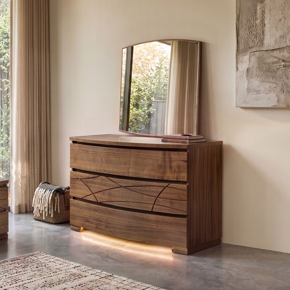 Frontansicht einer modernen, geformten Kommode aus Walnussholz mit unterer LED-Beleuchtung, SKU 8270D, gekrönt vom passenden modernen, geformten Spiegel, SKU 8275, in einem hellen, eleganten Schlafzimmer.