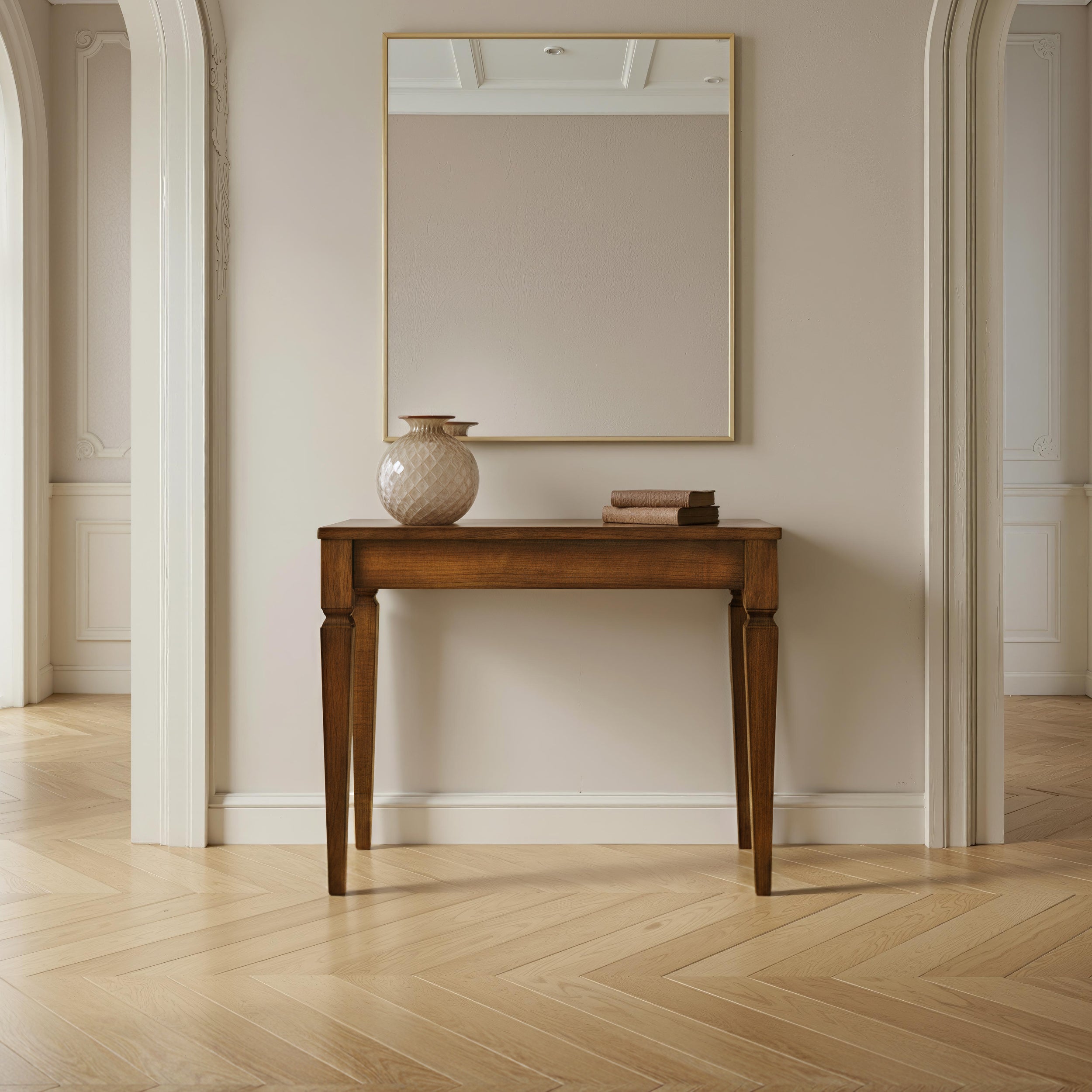 Consolle da ingresso Piombini modello Tiziano in legno con finitura Bassano Chiaro Anticato, fotografata frontalmente sotto un grande specchio in un ambiente classico luminoso con parquet, vaso e libri – RH970
