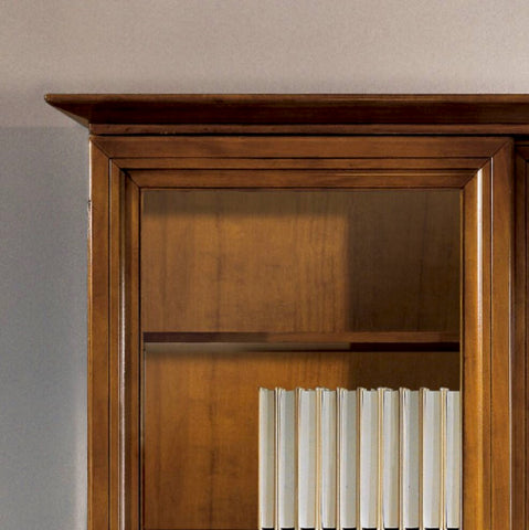 Dettaglio del cappello superiore della libreria classica D'Este Piombini P1017PMB, realizzato con cornici sagomate e lavorazione artigianale del legno. La struttura superiore dona slancio, equilibrio architettonico e prestigio alla composizione, valorizzando l'eleganza senza tempo del mobile.