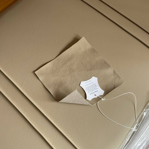 Detai  l of the Modigliani bed headboard upholstered in beige leather, with a leather sample applied and an ID tag. 1925–2025 centenary logo in the bottom right.