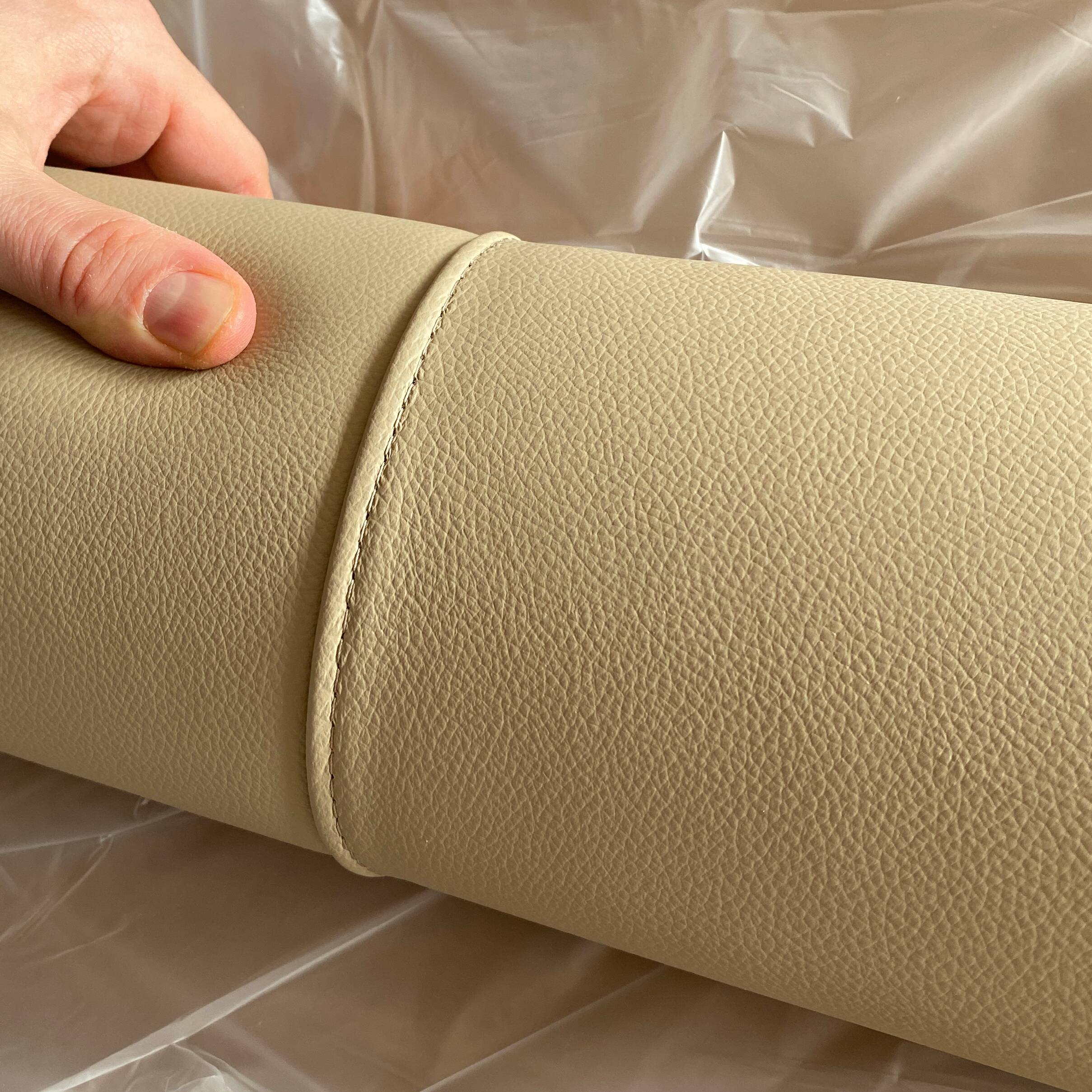 Dettaglio artigianale della cucitura della pelle beige utilizzata per il letto Modigliani. Una mano mostra la texture e la precisione della lavorazione.