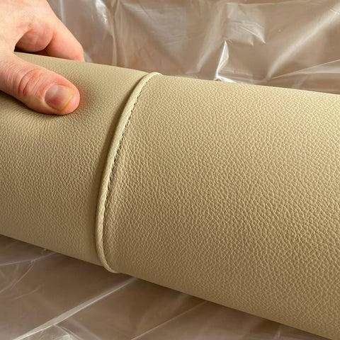 Handcrafted detail of the beige leather stitching used for the Modigliani bed. A hand shows the texture and precision of the craftsmanship. 1925–2025 centenary logo in the lower right.