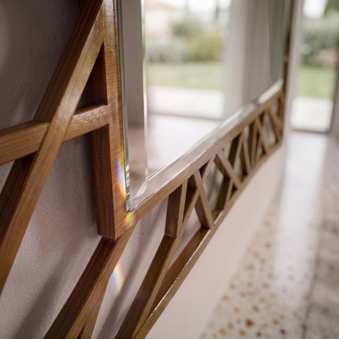 Primo piano dettaglio dell'angolo e del bordo della specchiera classica rettangolare traforata Visconti Piombini in ciliegio, che mostra la lavorazione del legno e lo smusso dello specchio con un effetto luce arcobaleno.